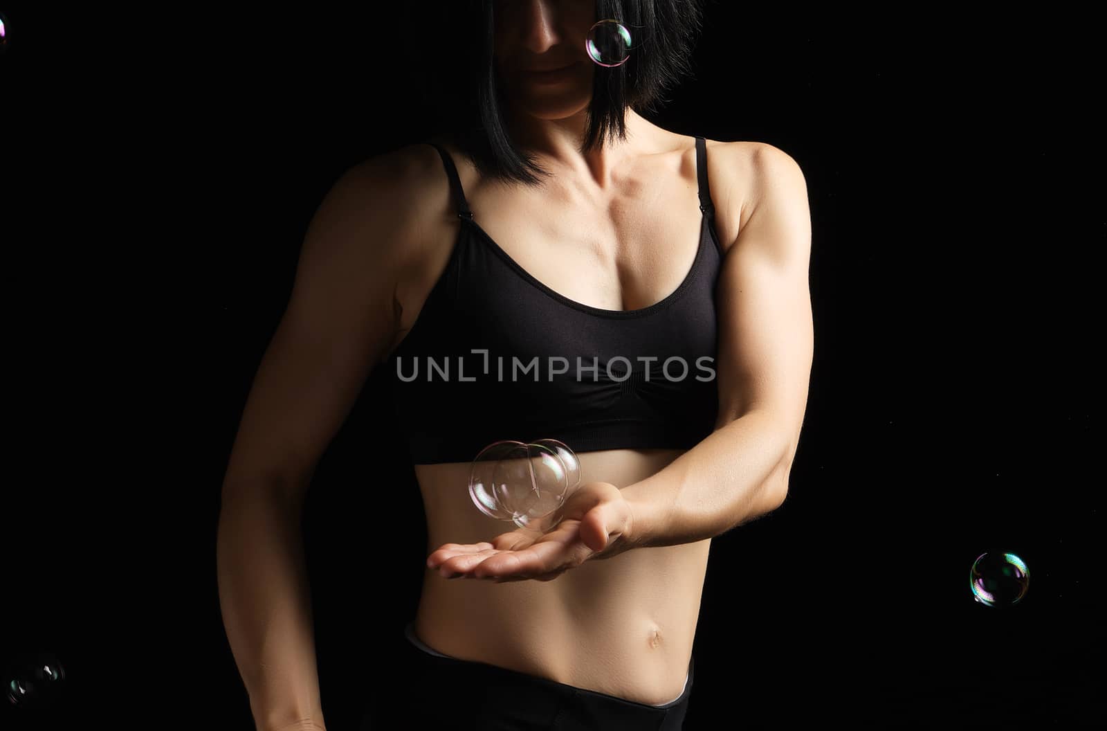 girl with a sports figure and muscles holds a soap bubble in her by ndanko