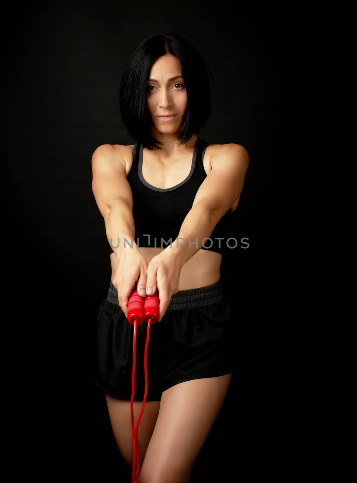 young woman with a sports figure in black uniform holds a red rope for jumping, low key
