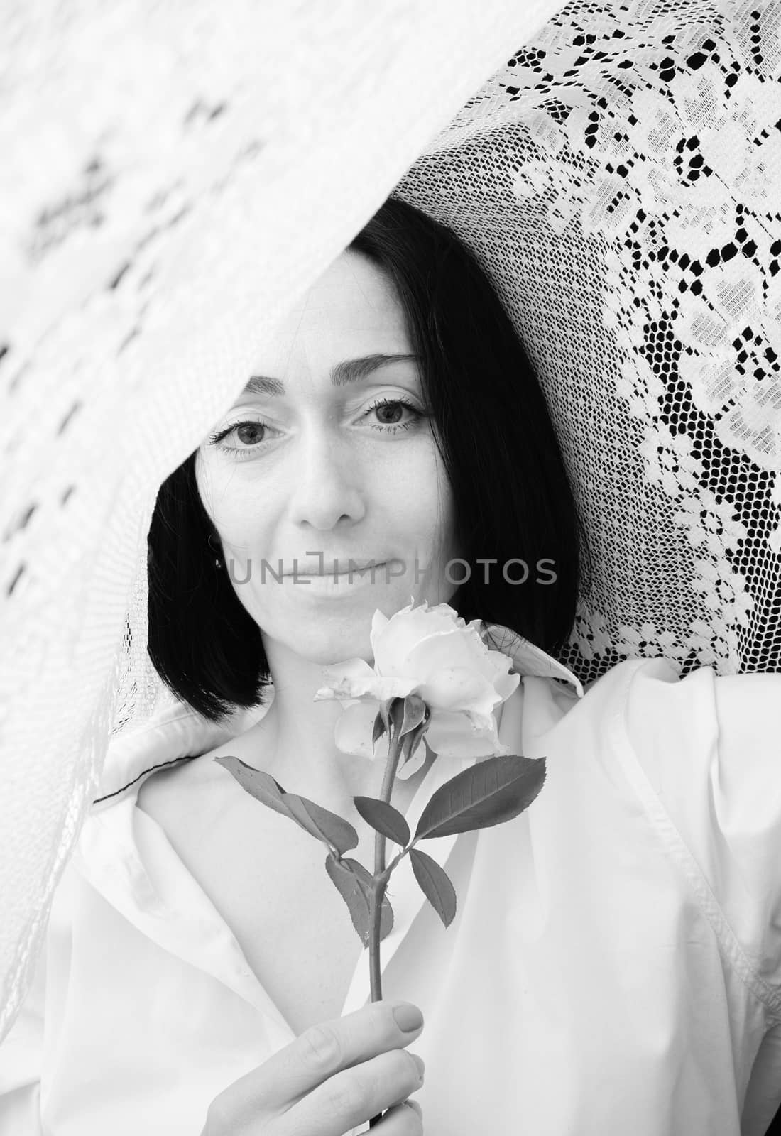 portrait of a young woman with a white rose in her hands surrounded by lace white curtains, black and white tinting