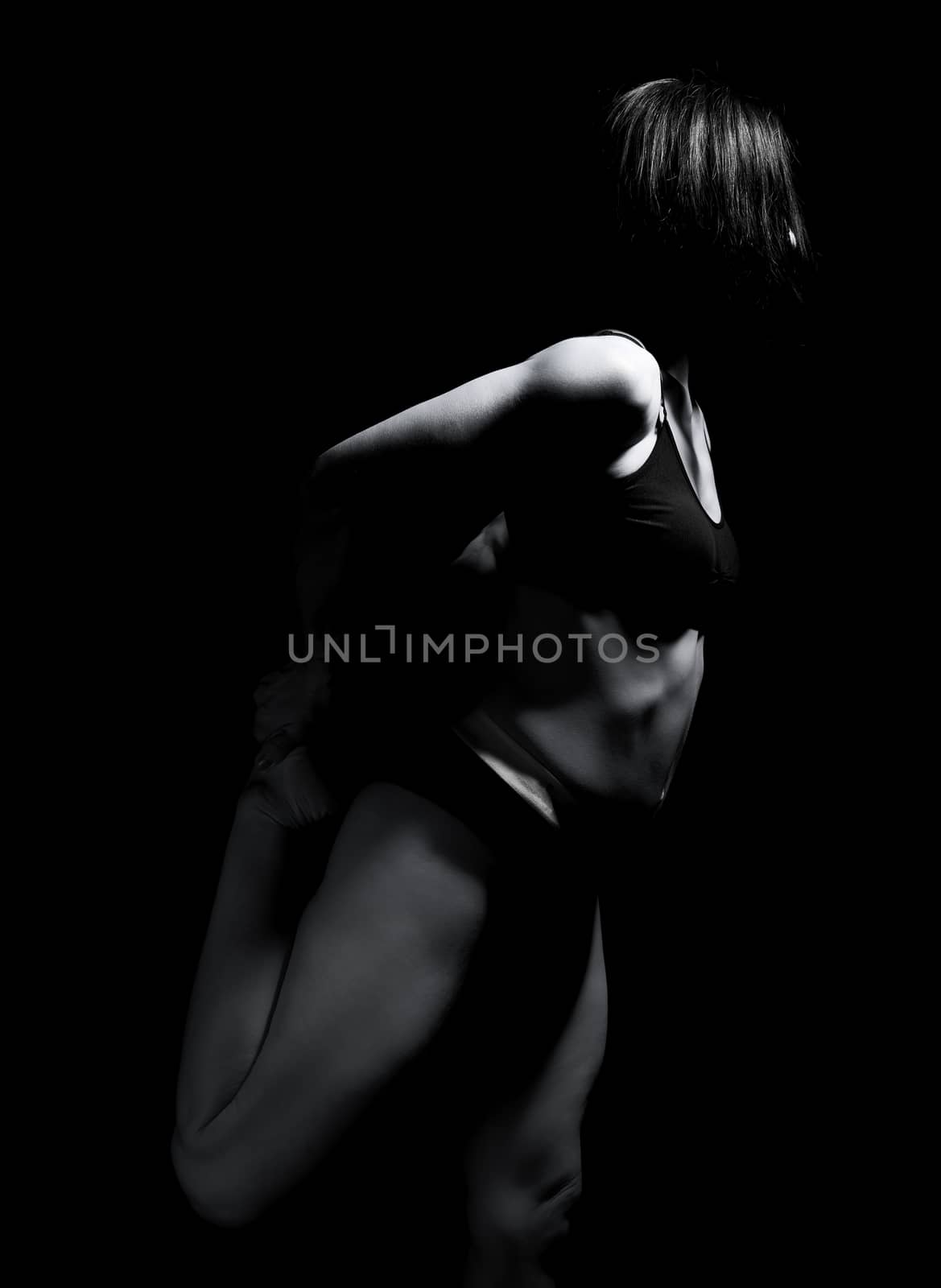 beautiful athletic woman with a muscular body is dressed with a black topic and shorts stands sideways, leg bent back, black and white tinting