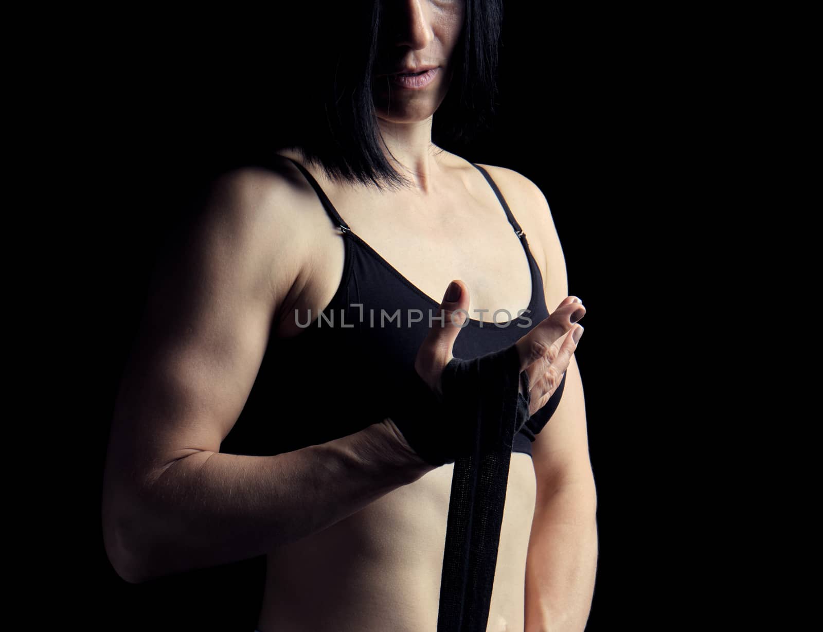 beautiful athletic girl with black hair rewinds her hand with a black elastic bandage before training,  dark background