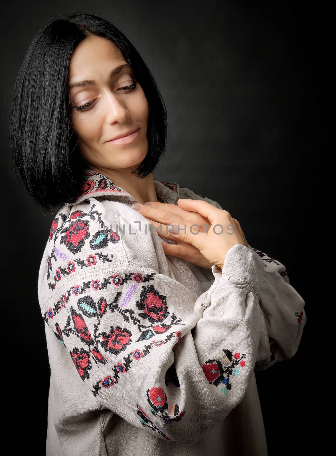 beautiful young woman in an embroidered ancient Ukrainian dress with a cross-stitch on a black background, linen clothes, look down