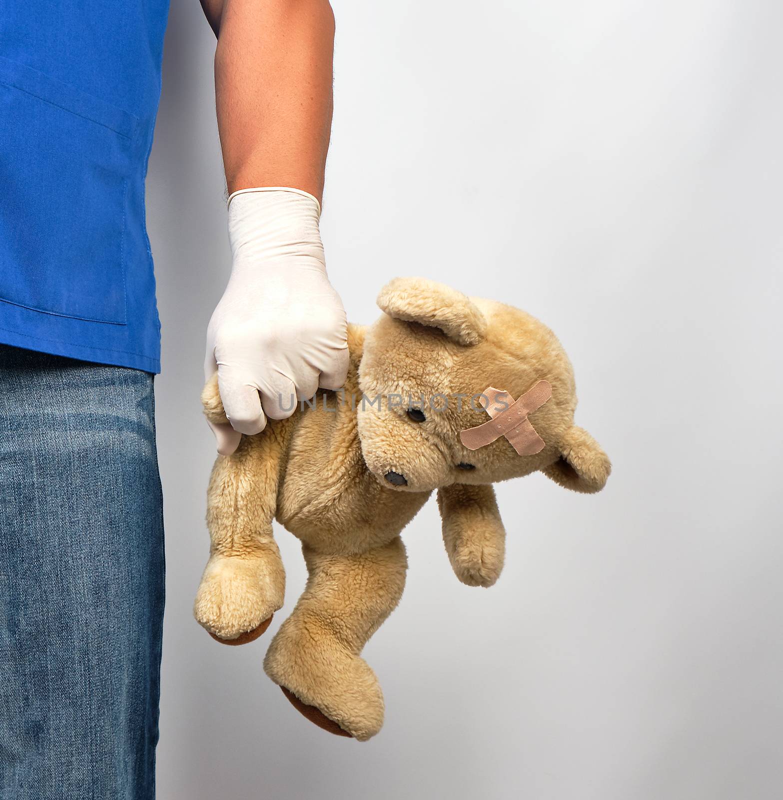 doctor in blue uniform and white latex gloves holding a brown teddy bear, pediatrics concept, copy space 