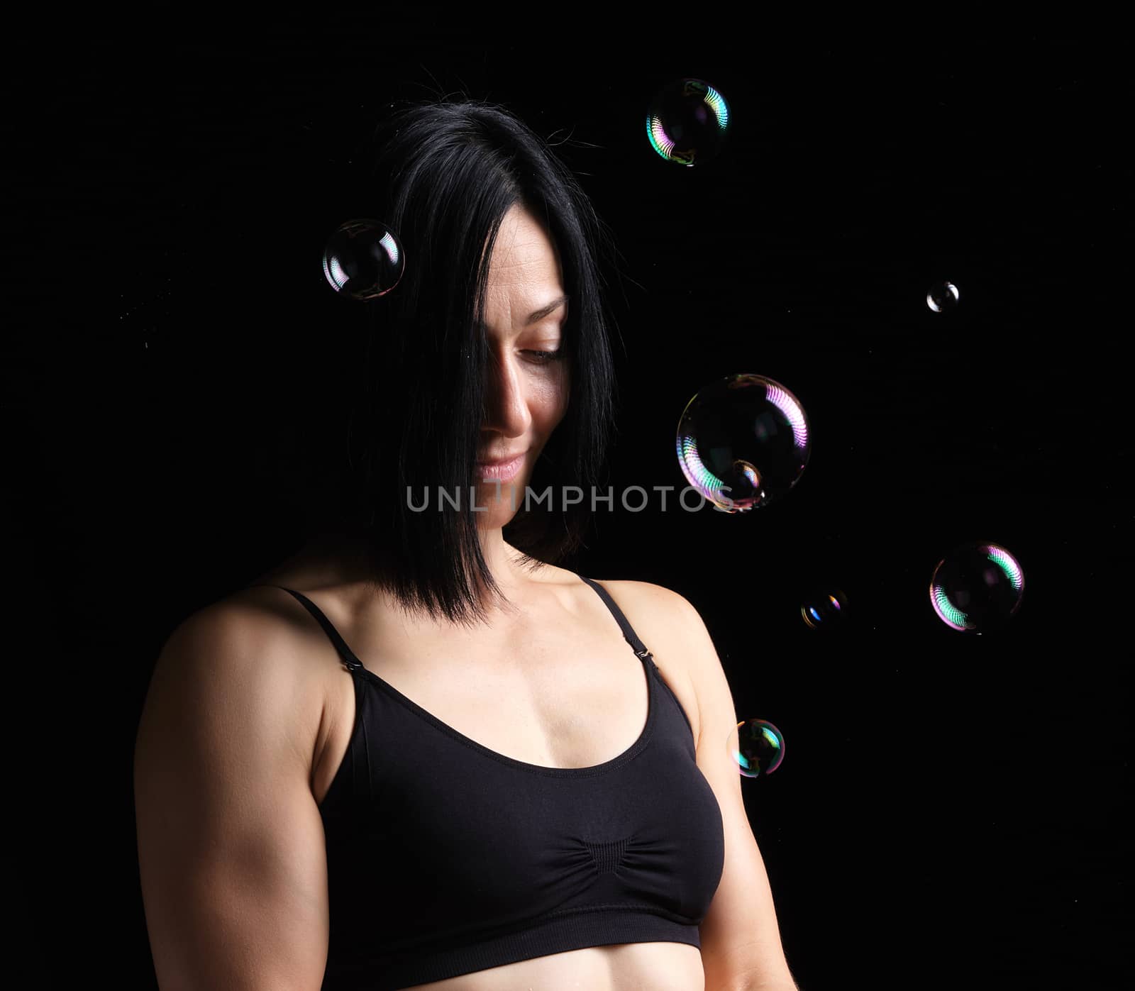 portrait of a young girl with black short hair and a sports figure on a dark background, flying soap bubbles around