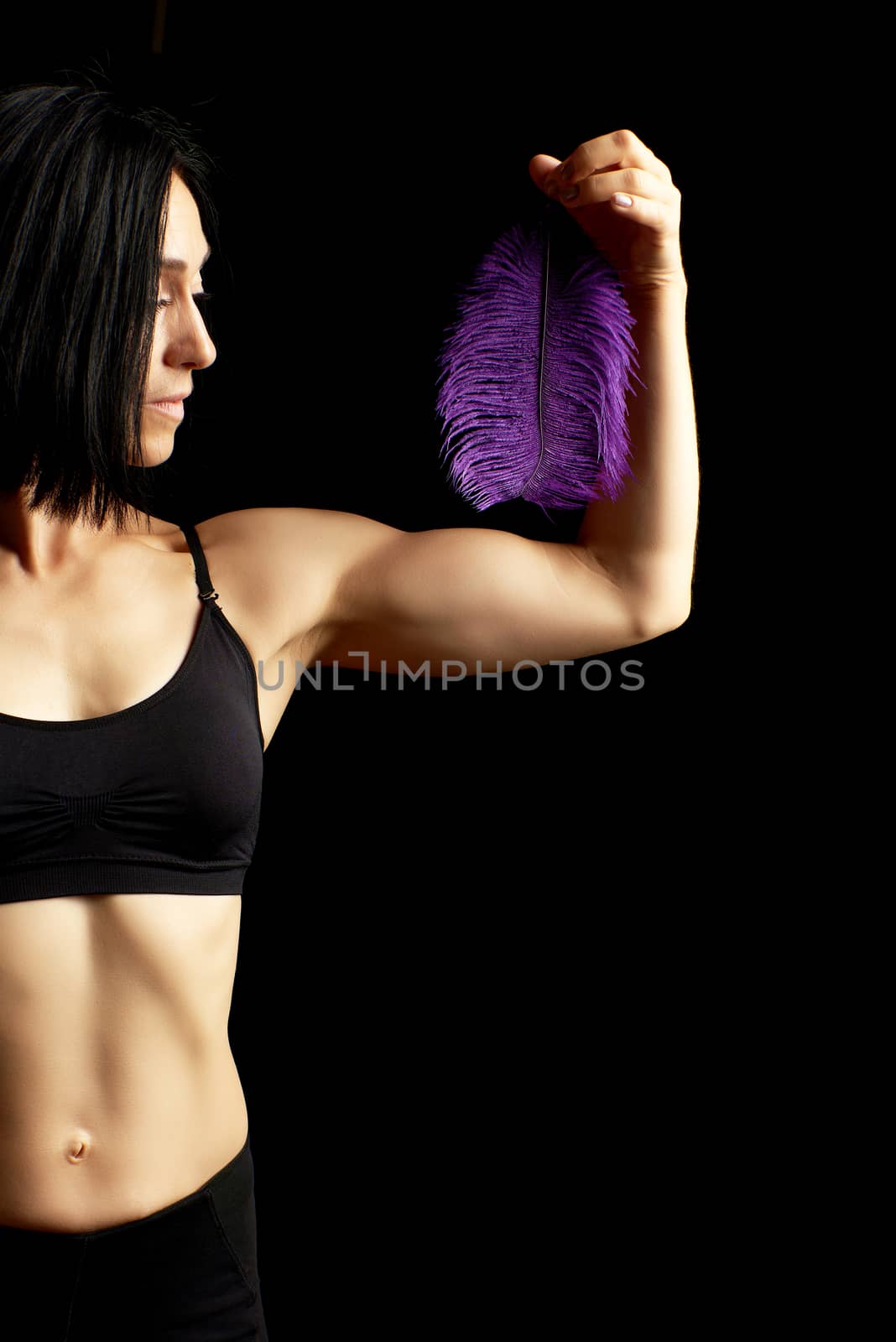 young woman with a sports figure and muscles dressed in black clothes holds a purple feather in her left hand, athlete with black hair, low key