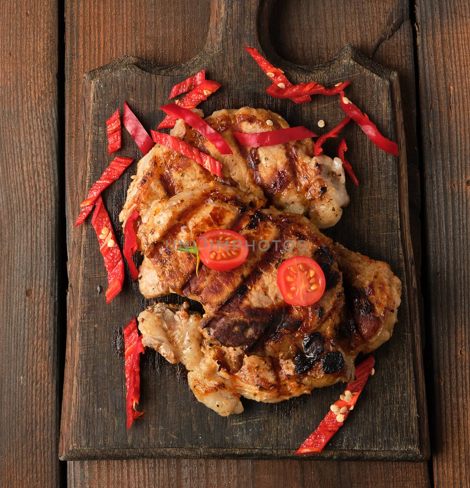 grilled pork pieces of meat on a grill lie on a vintage wooden board, close up