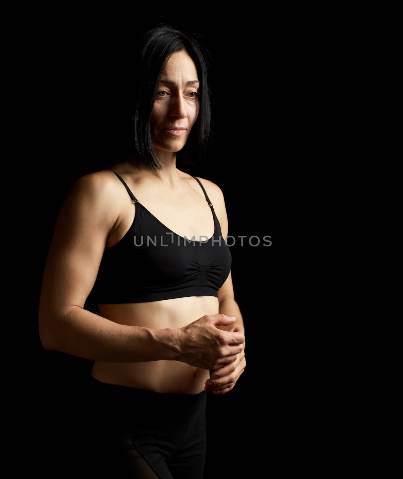 young girl with black hair athletic appearance stands on a dark background and looks away