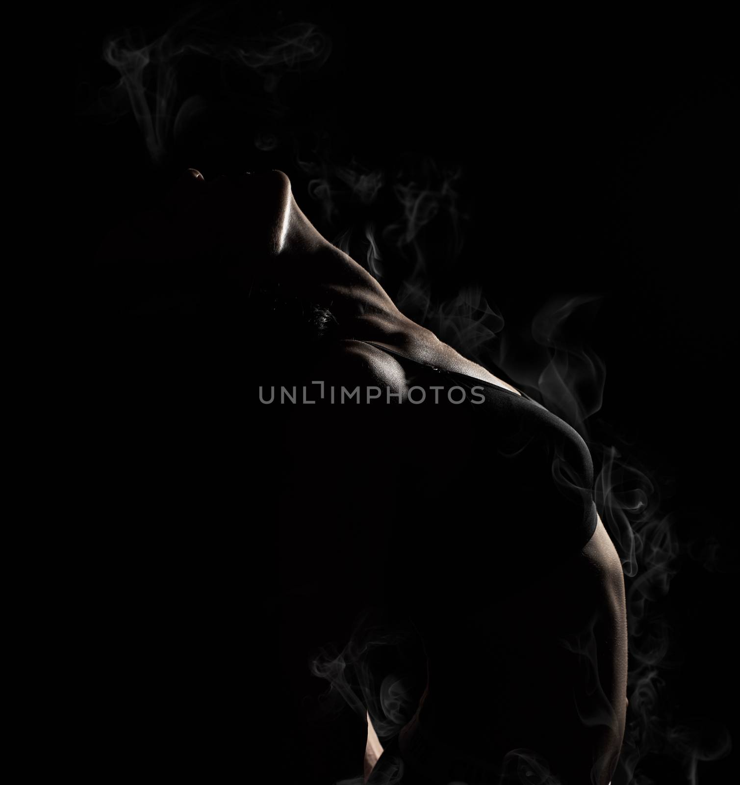 young beautiful athletic girl with muscles in a black bra bent the body back, white smoke vapor envelops the body