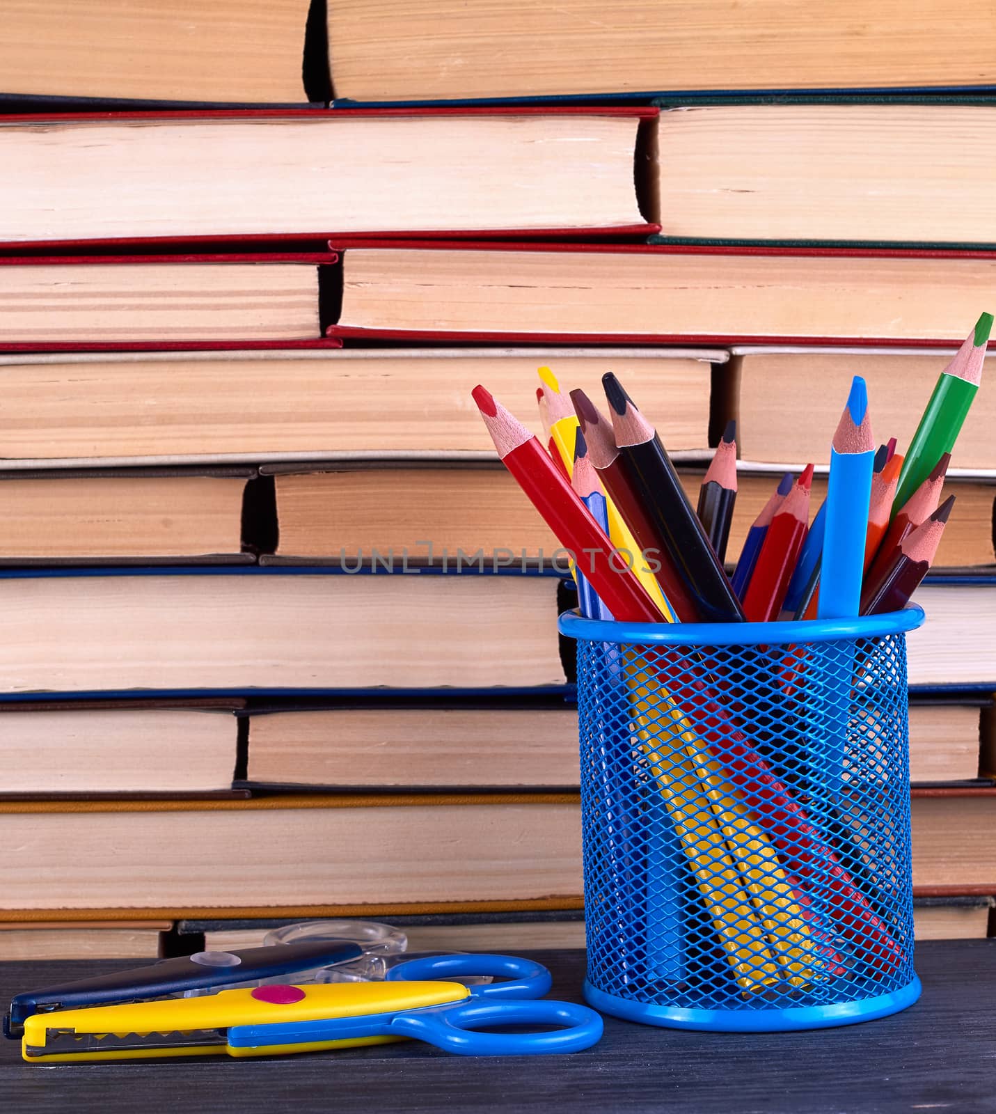 stacks of various hardback books and blue stationery glass with multi-colored wooden pencils, back to school concept 