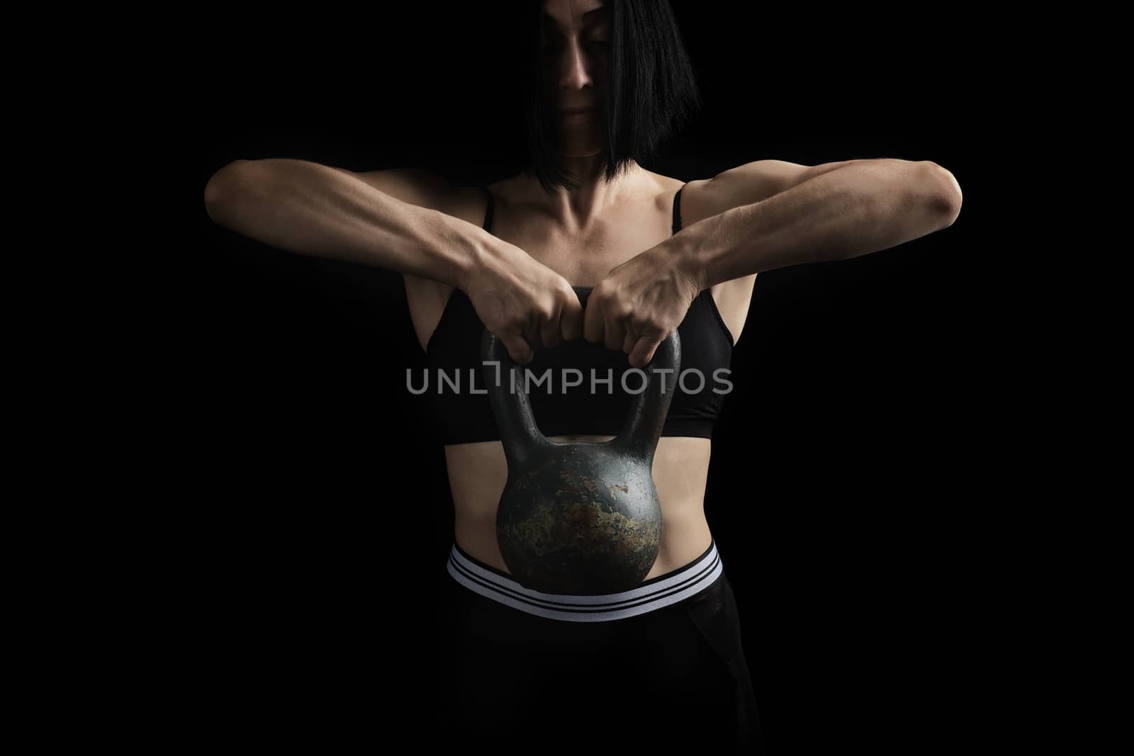 beautiful athletic girl with black hair raised with two hands a metal weight on a dark background, strength exercises
