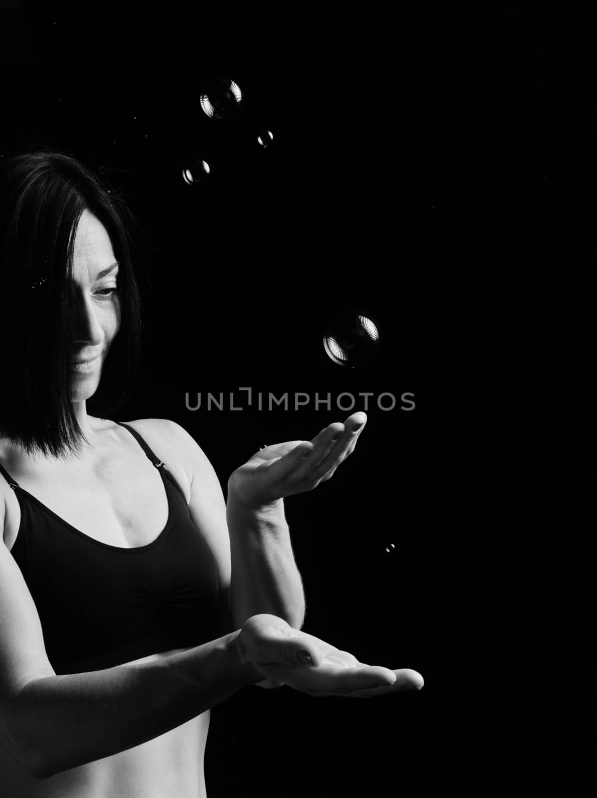 beautiful athletic woman with muscular body dressed with a black topic catches soap bubbles on a black background, studio portraits in a low key