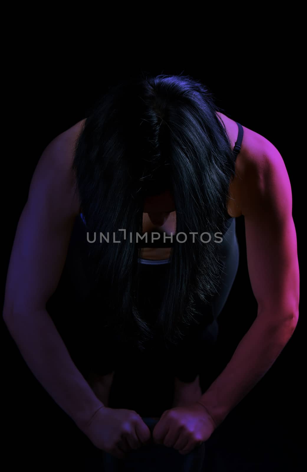 young girl of athletic appearance with black hair is pushing up from an iron kettlebell from a lying position, low key