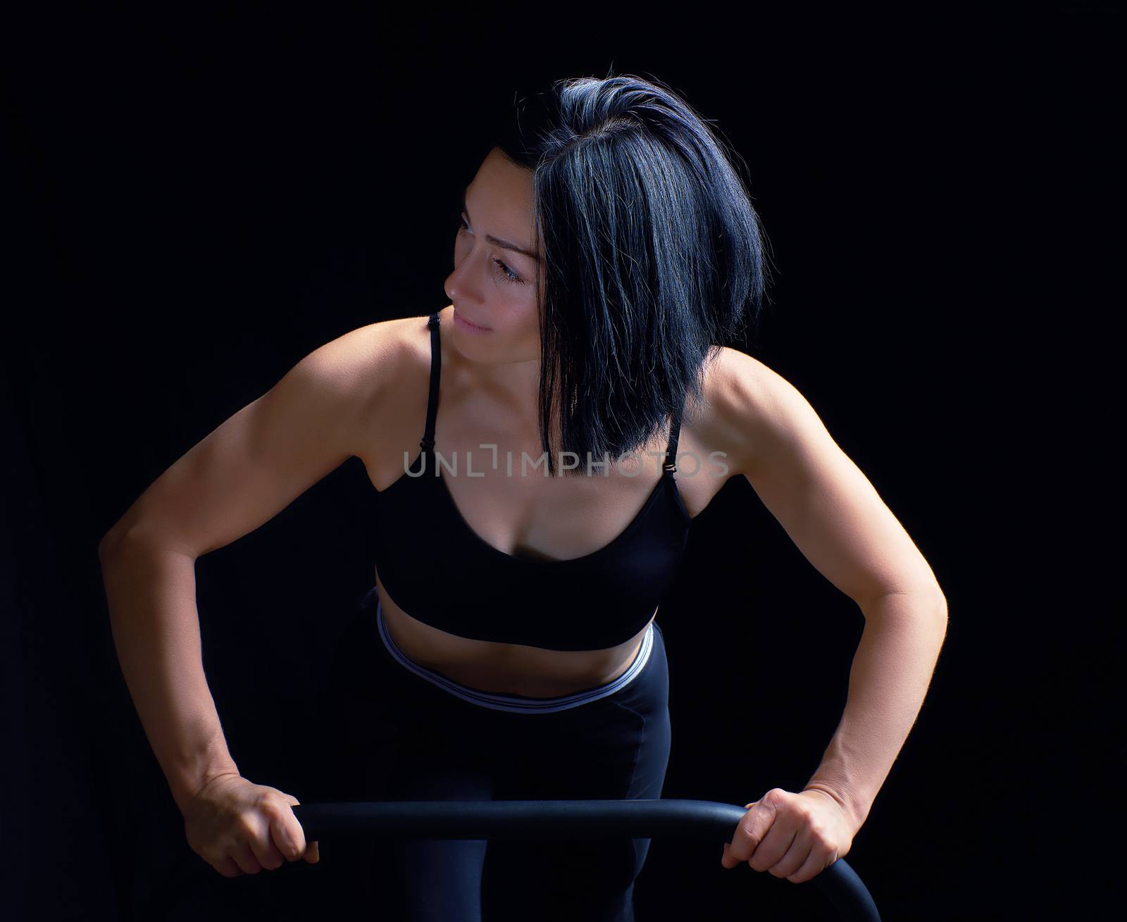 young beautiful athletic girl with muscles in a black bra is wrung out in her arms, doing fitness and sports, studio photo in a dark key