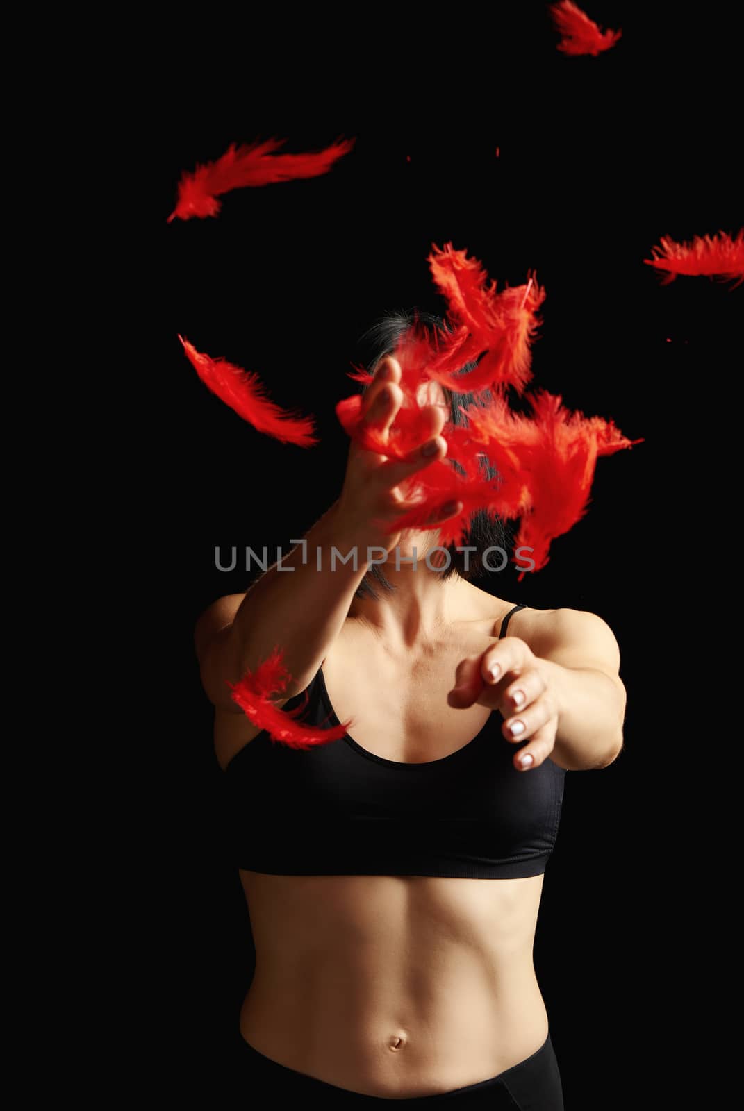 young beautiful athletic girl in black clothes throws up red feathers, arms raised up, low key
