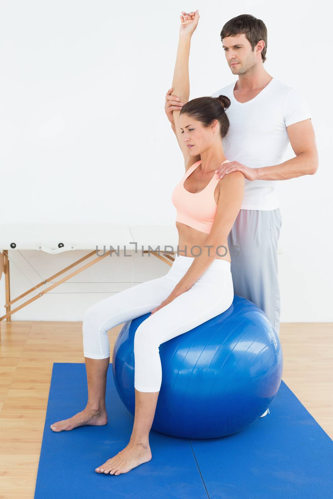 Woman on yoga ball while working with physical therapist by Wavebreakmedia