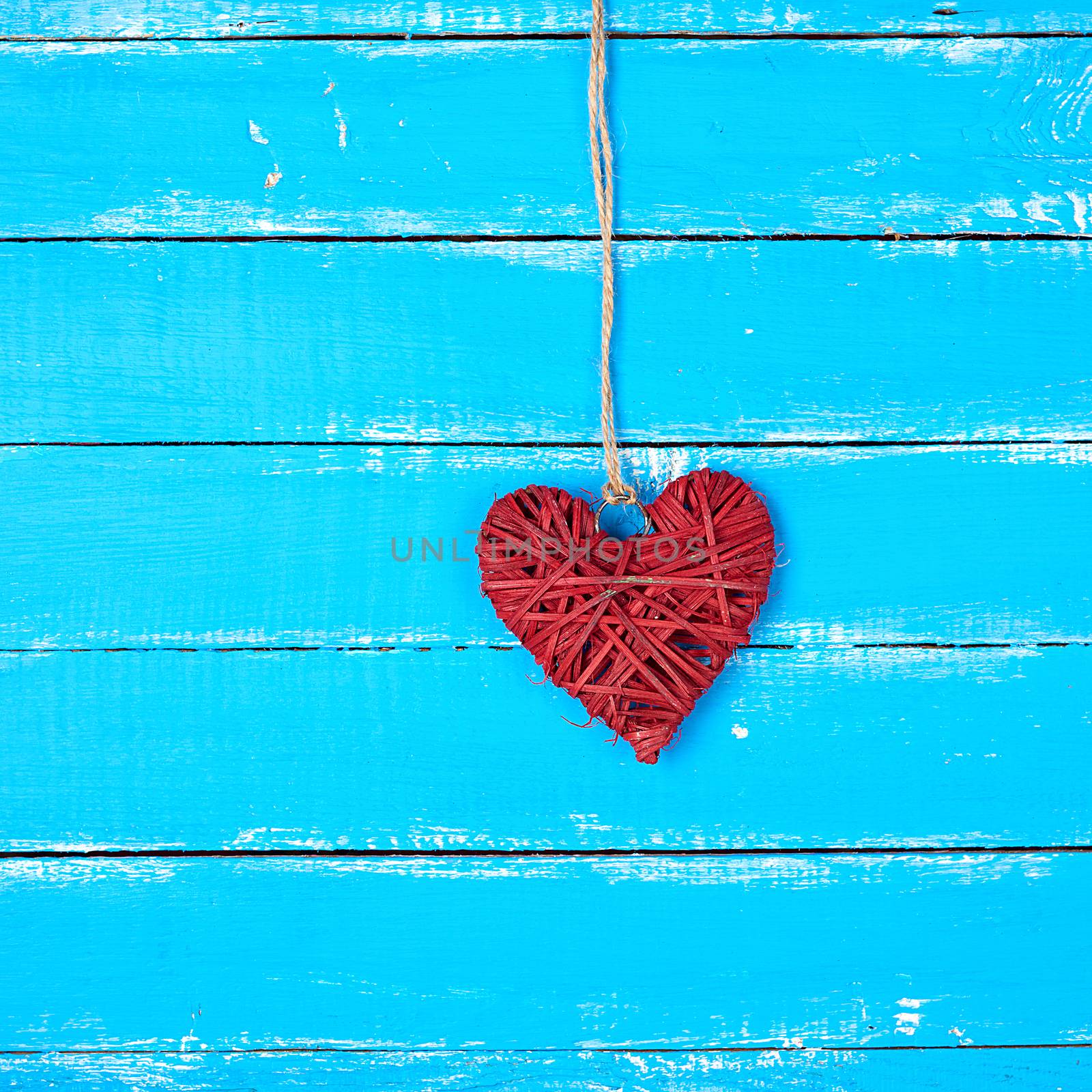 red  wicker decorative heart  hanging on a rope, blue wooden background, festive backdrop