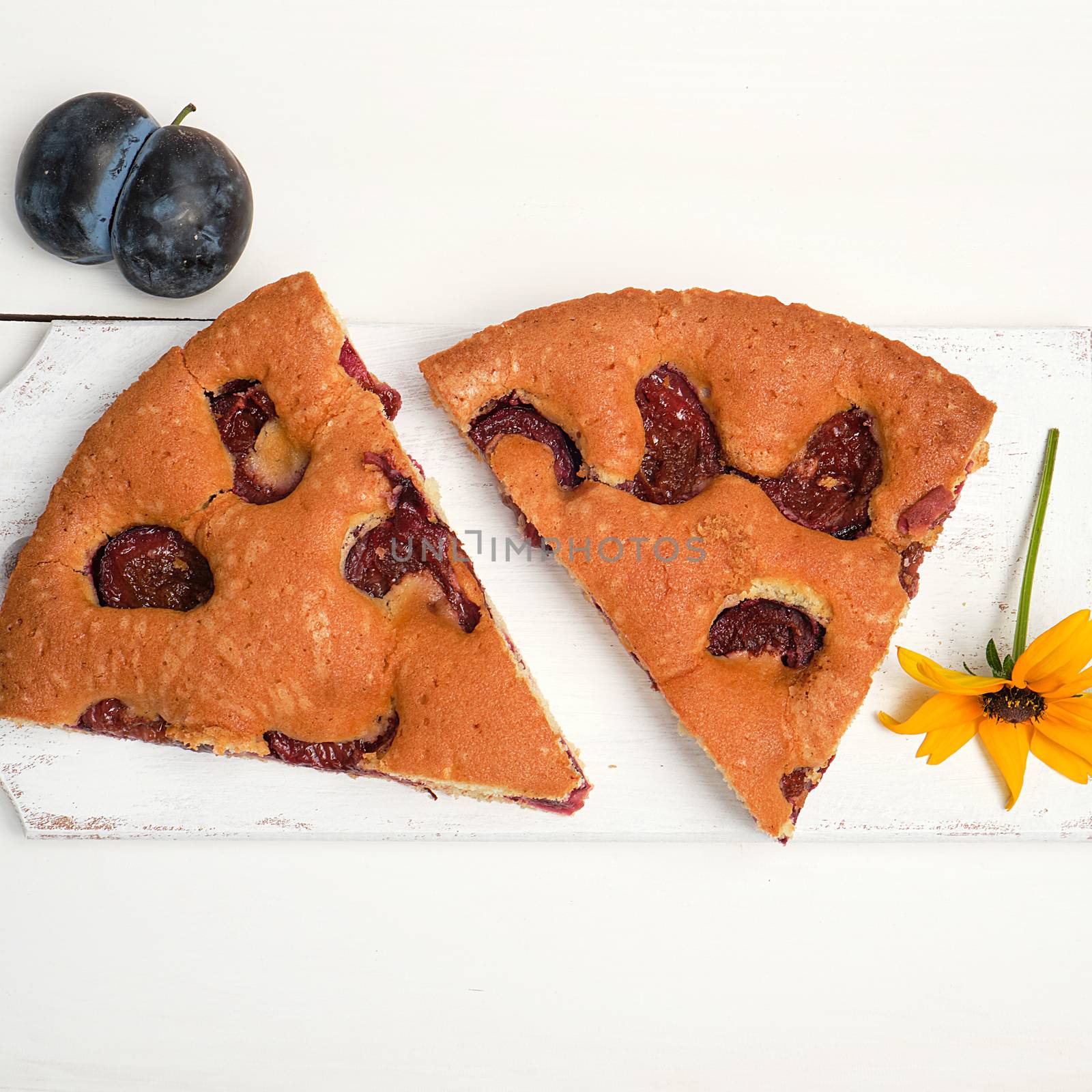 slices of biscuit plum cake on a white wooden board and fresh fruits, top view