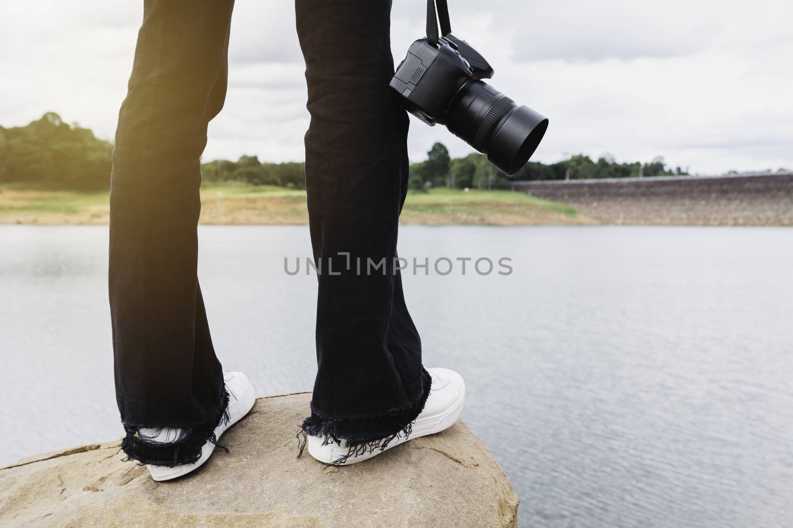 Photographer standing on a rock and holding a camera. Woman standing on rock near river.