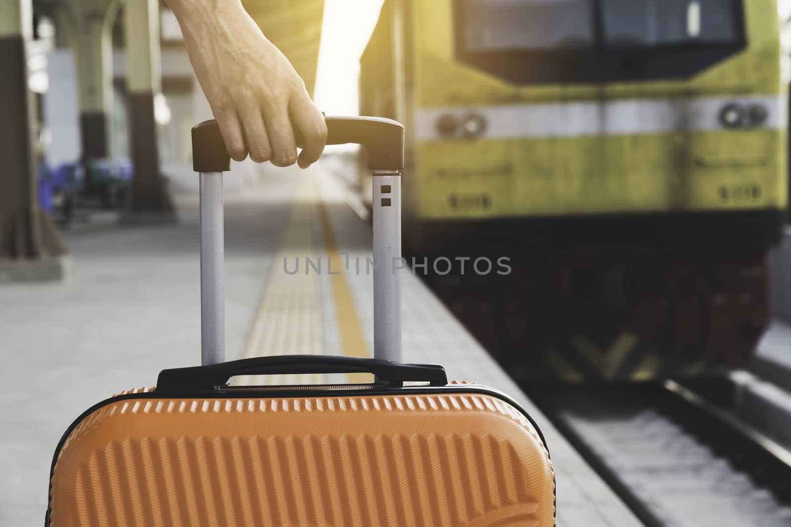 Woman dragging orange suitcase luggage bag, walking in train station. Travel concept.