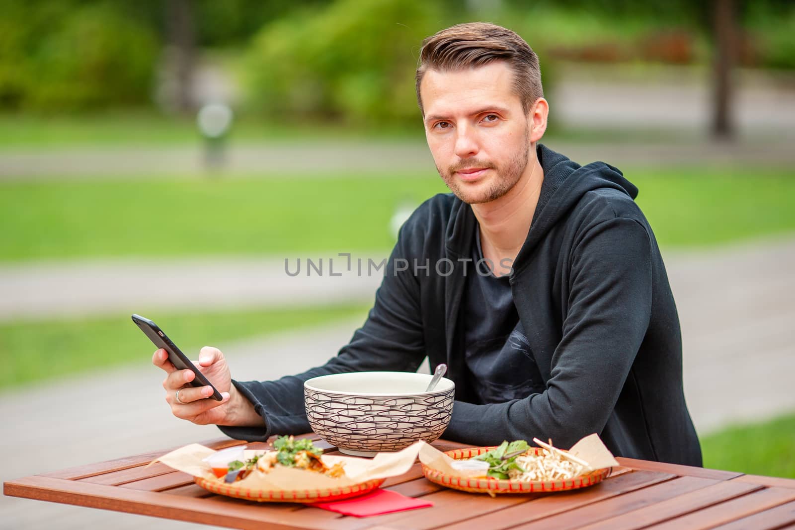 Young man eating take away noodles on the street by travnikovstudio