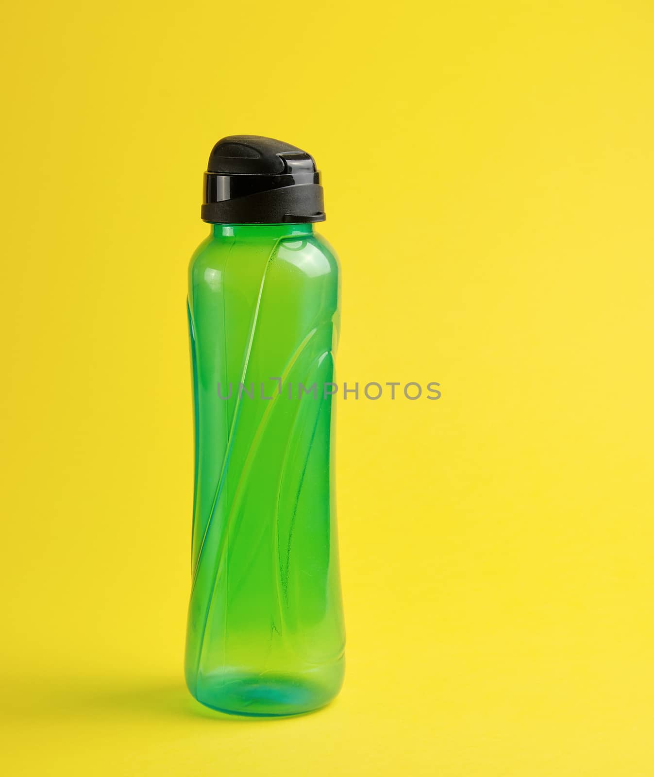 closed plastic green transparent sports bottle on a yellow background, close up