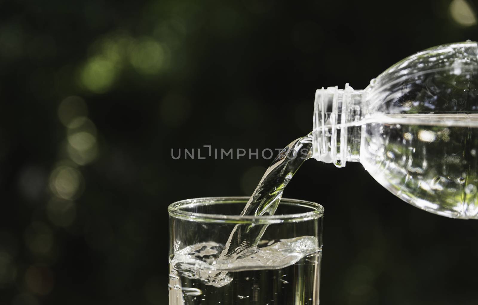 Pouring water from bottle into the glass on blurred background.