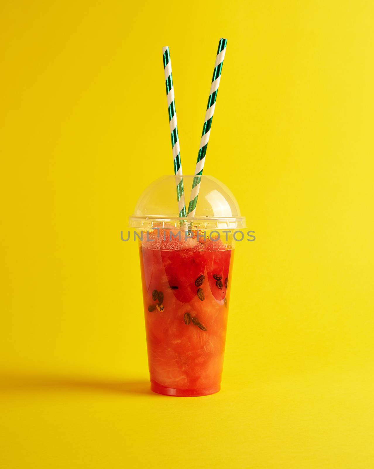smoothie from ripe red watermelon in a plastic cup,  two paper tubes  on a yellow background