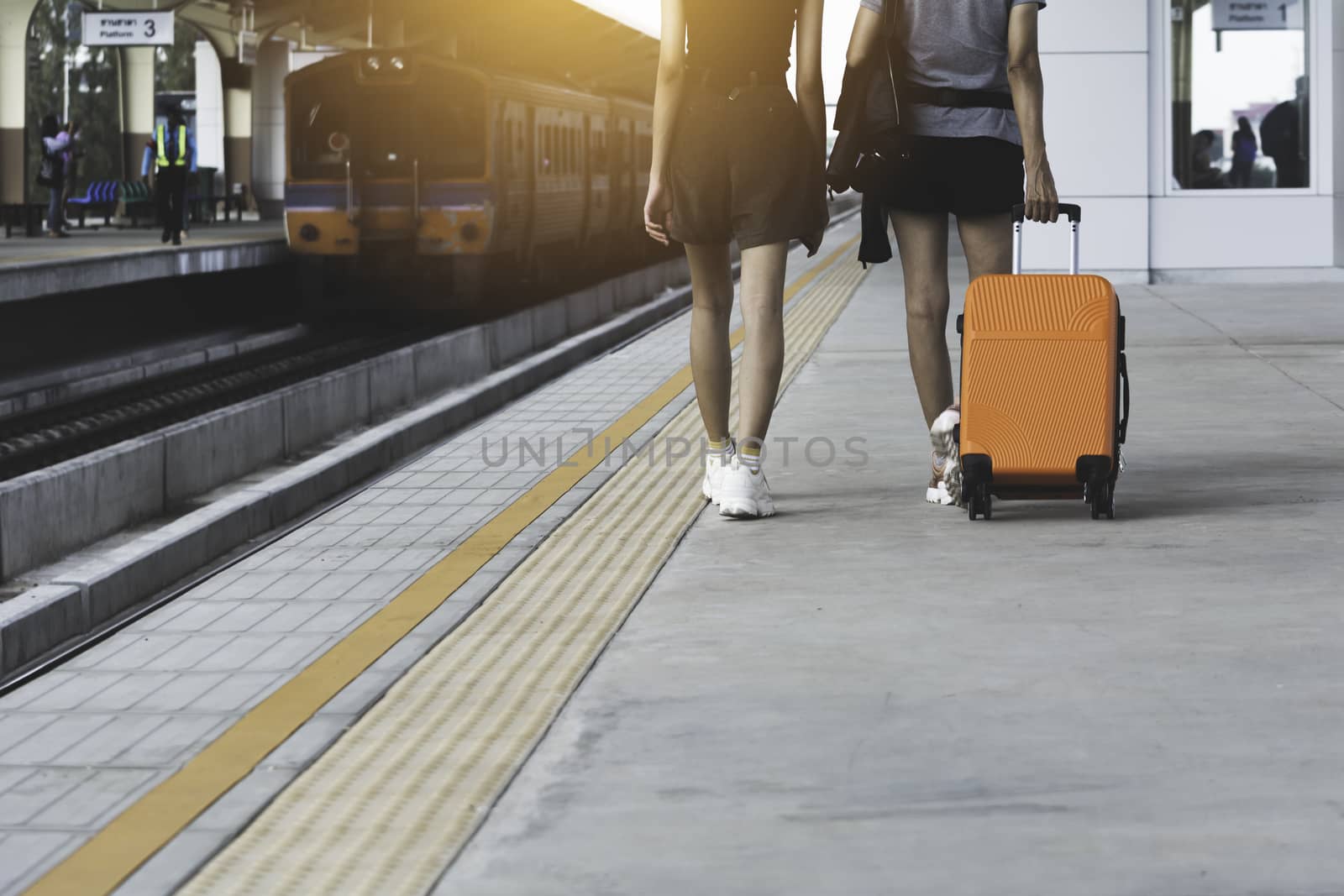 Woman dragging orange suitcase luggage bag, walking in train station. Travel concept.