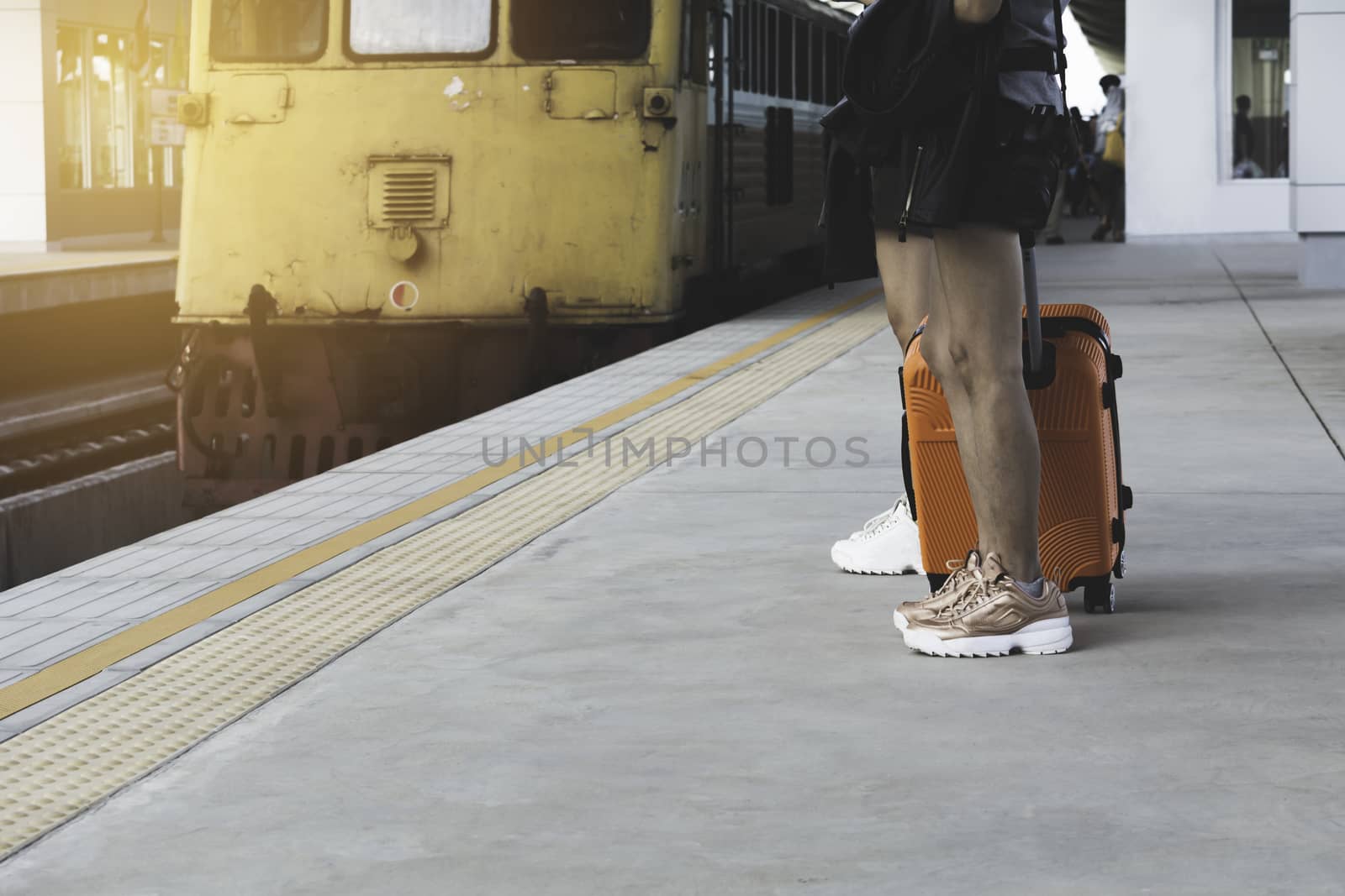 Woman dragging orange suitcase luggage bag, walking in train station. Travel concept.