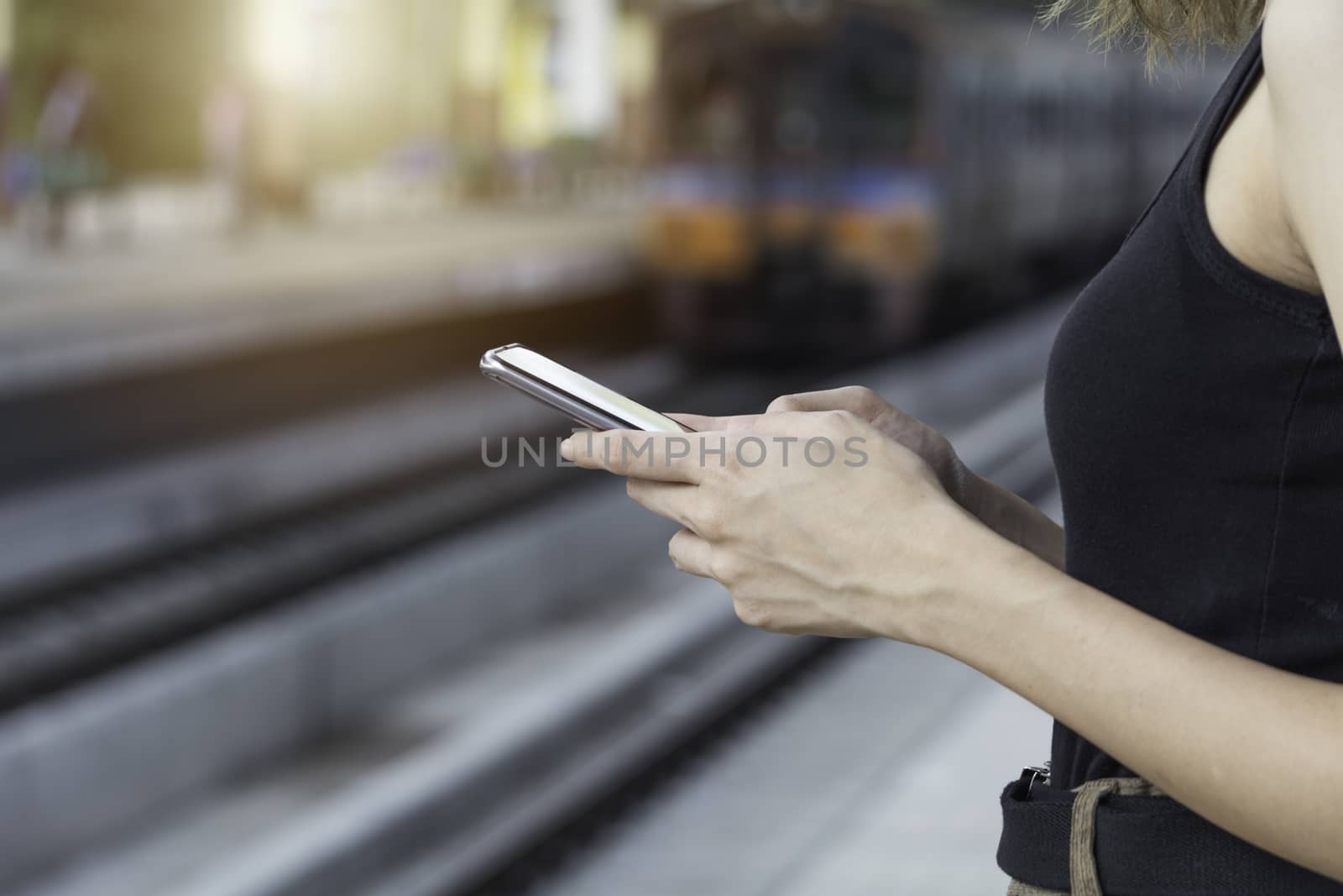 Woman standing and waiting for train and using smart phone in train station. Travel concept.