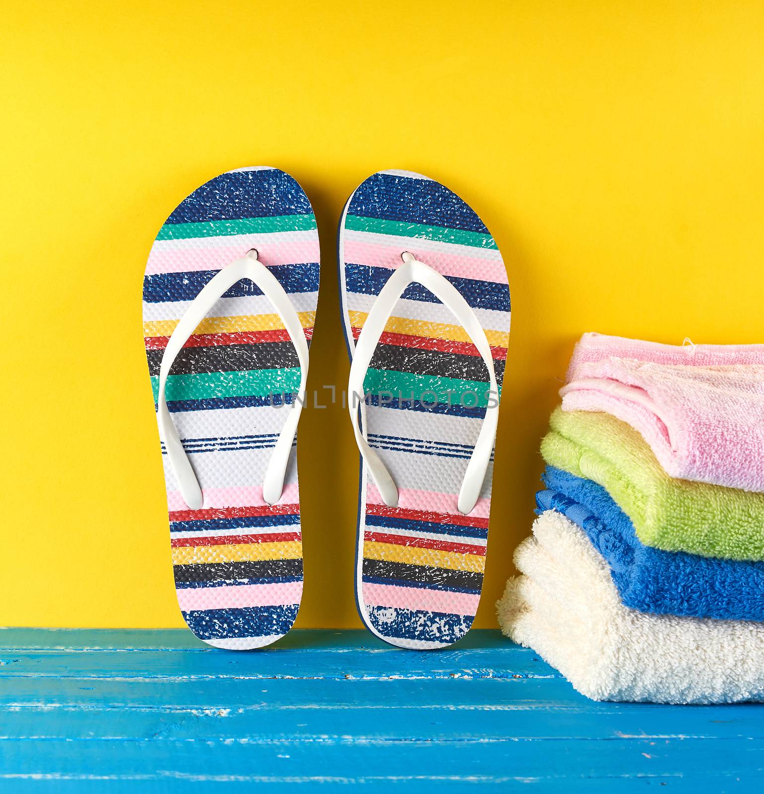 pair of female beach slippers and a  towels  on a blue yellow background,  concept of a vacation at sea