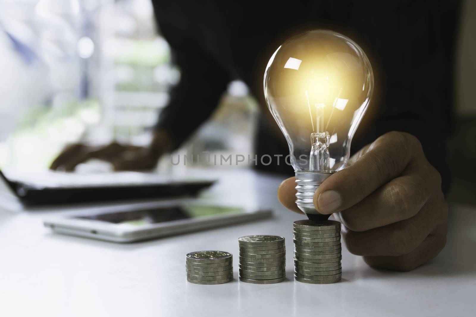Hand of male holding a light bulb with stack of coins and copy space for accounting, ideas and creative concept.