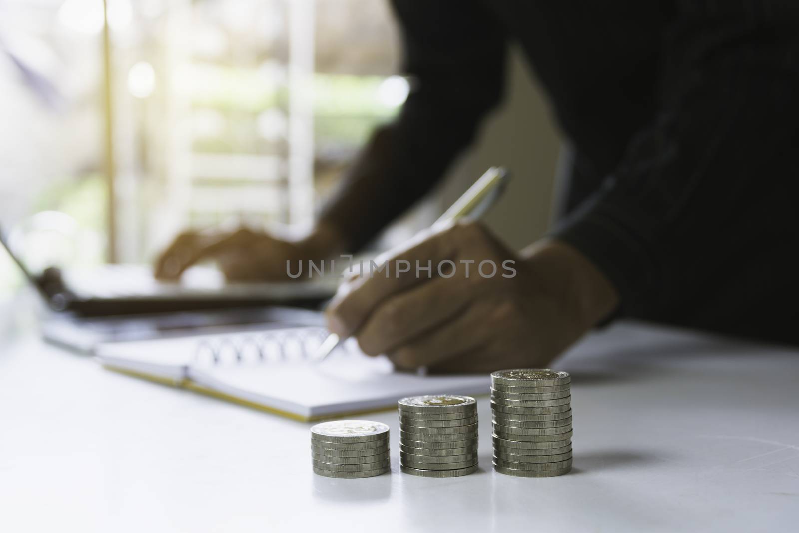 Person working and writing on notebook with stack of coins for f by kirisa99