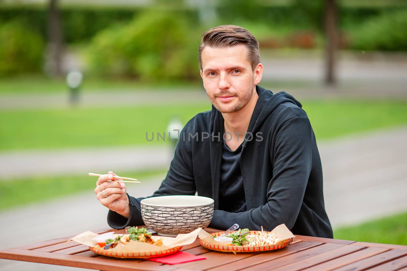 Young man eating take away noodles on the street by travnikovstudio