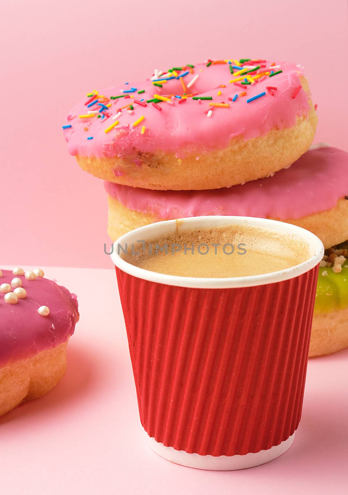 round red glazed donut and paper cup with coffee on a pink background, close up