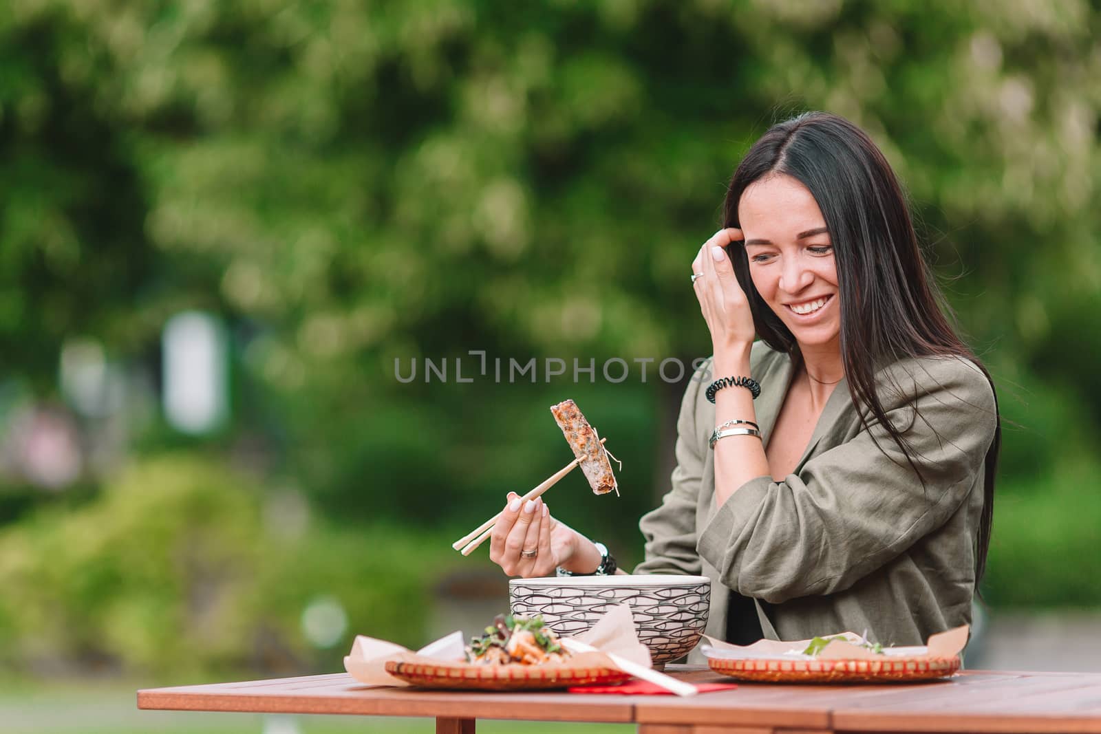 Young woman eating take away noodles on the street by travnikovstudio