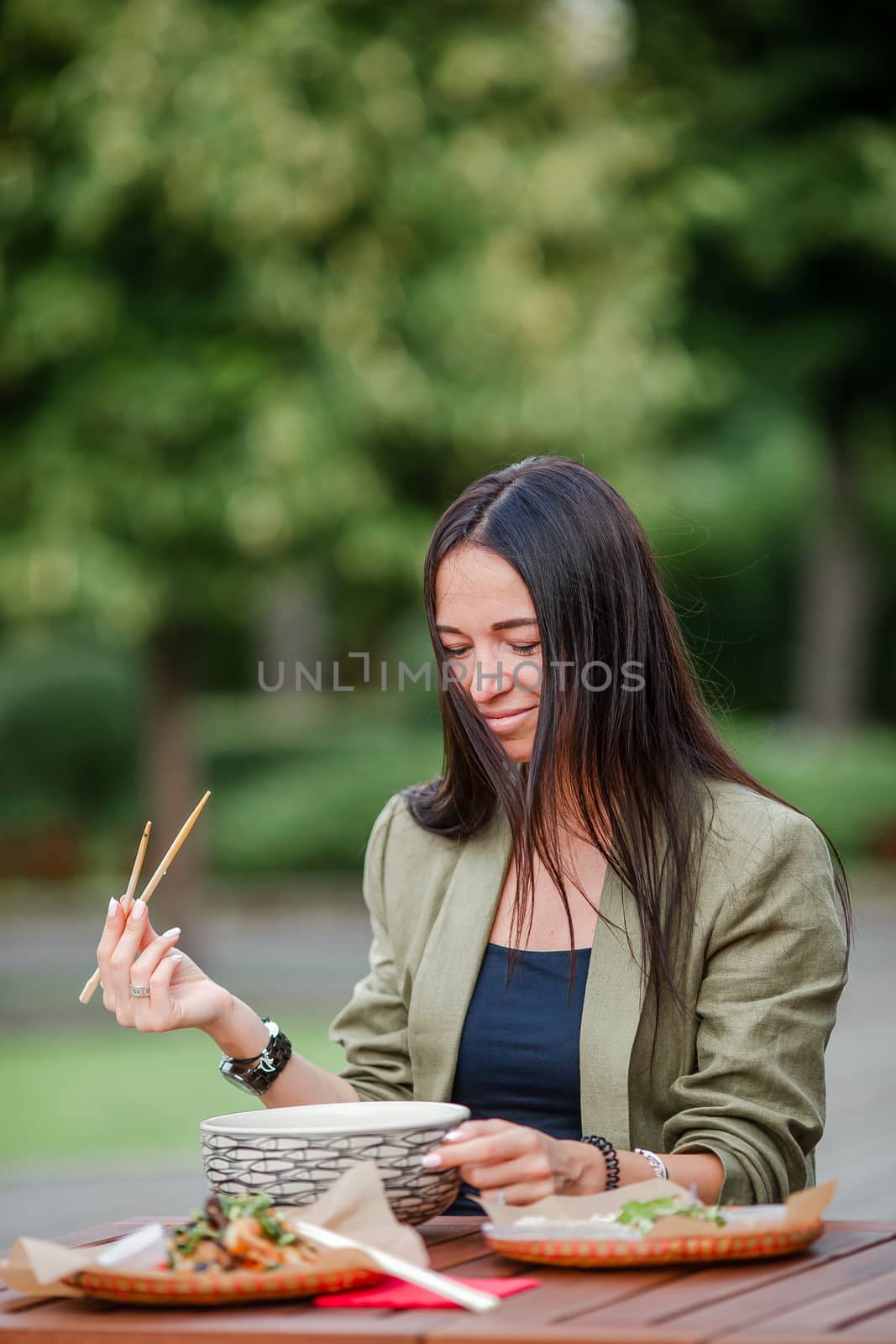 Young woman eating take away noodles on the street by travnikovstudio