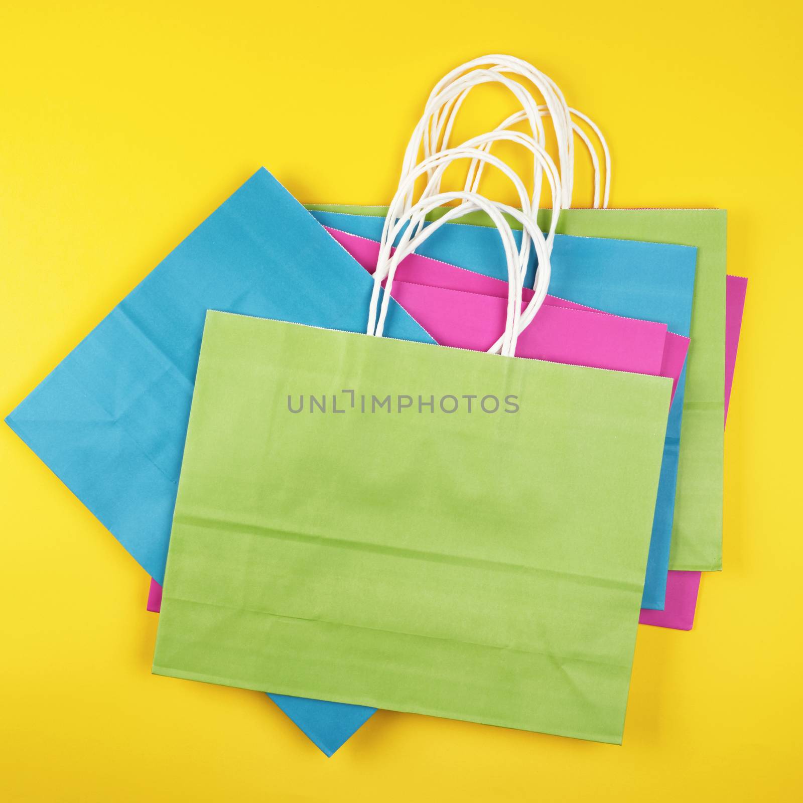 stack rectangular multi-colored paper shopping bags with white handles on a yellow background, flat lay