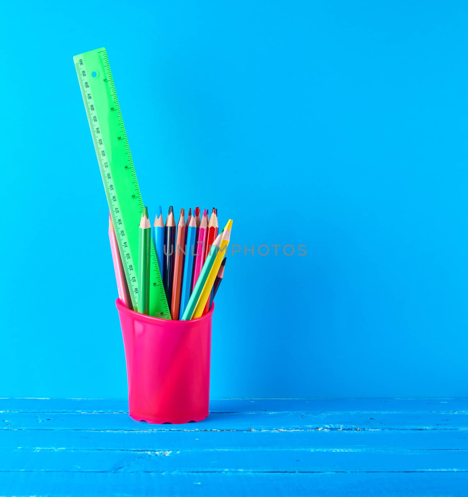 pink stationery glass with multi-colored wooden pencils and , blue background, copy space