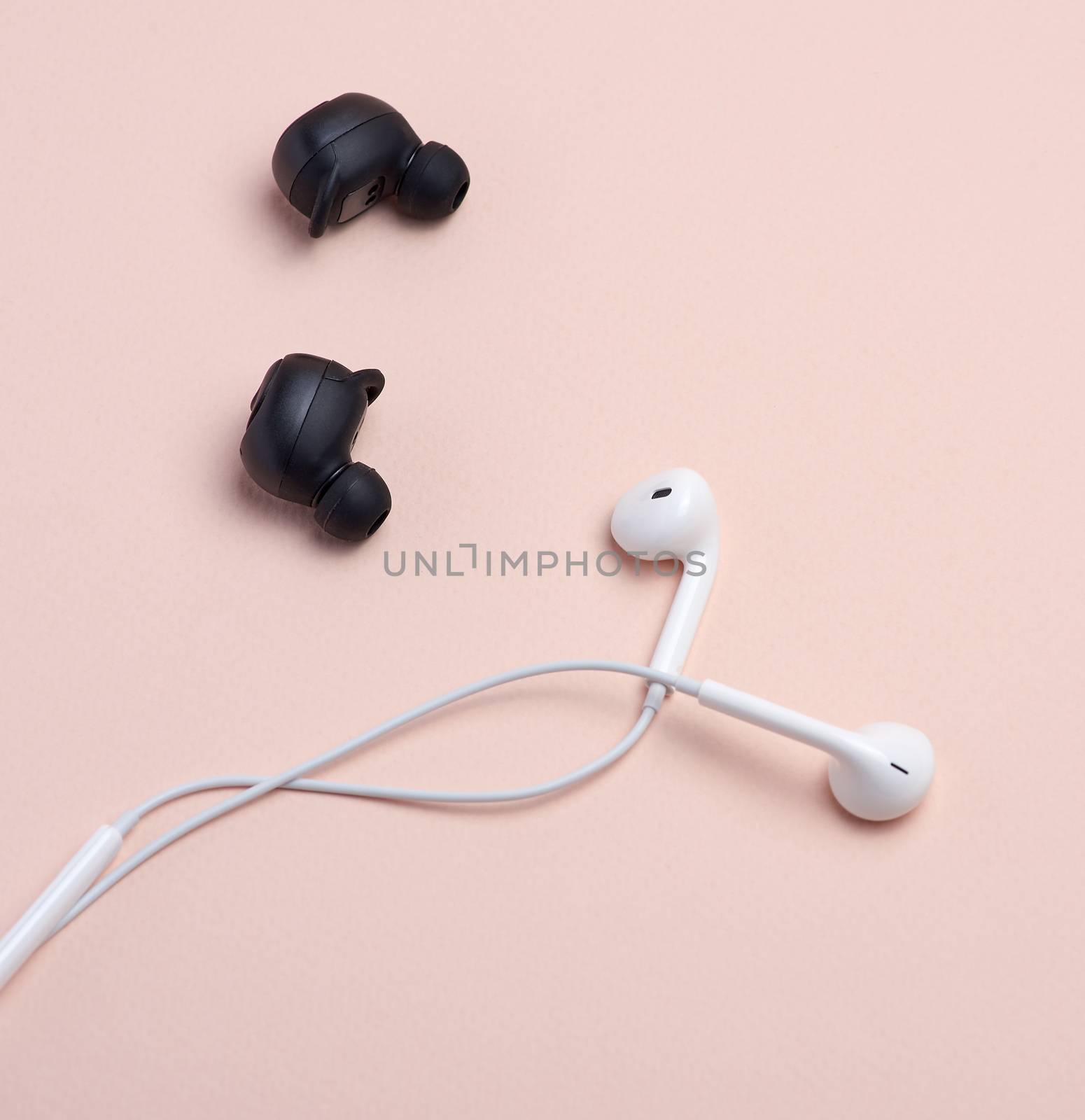 black wireless and white earphones with wire on a beige background, technology concept