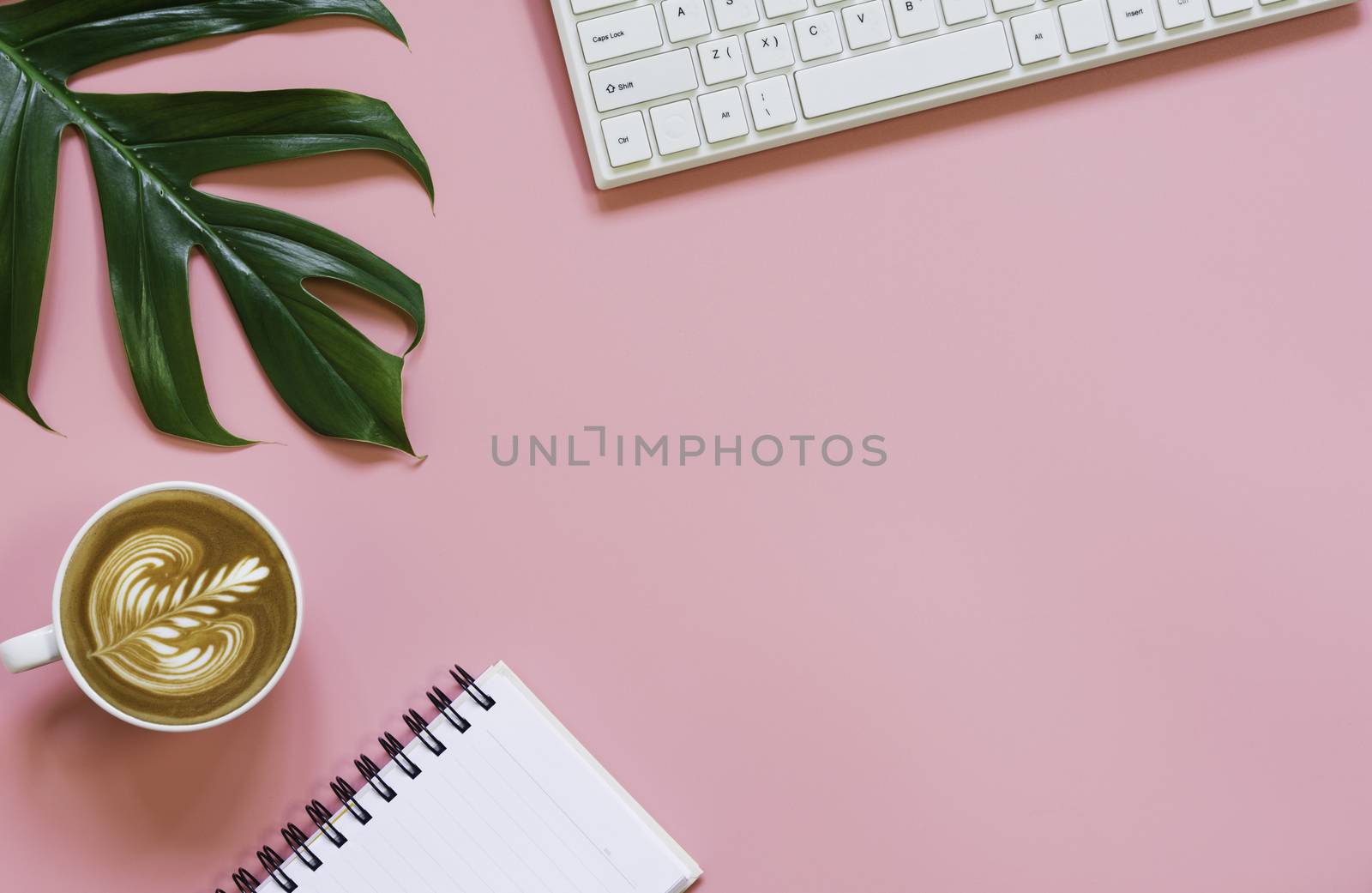 A cup of coffee with keyboard and copy space on pink background. Office desk and drink concept.