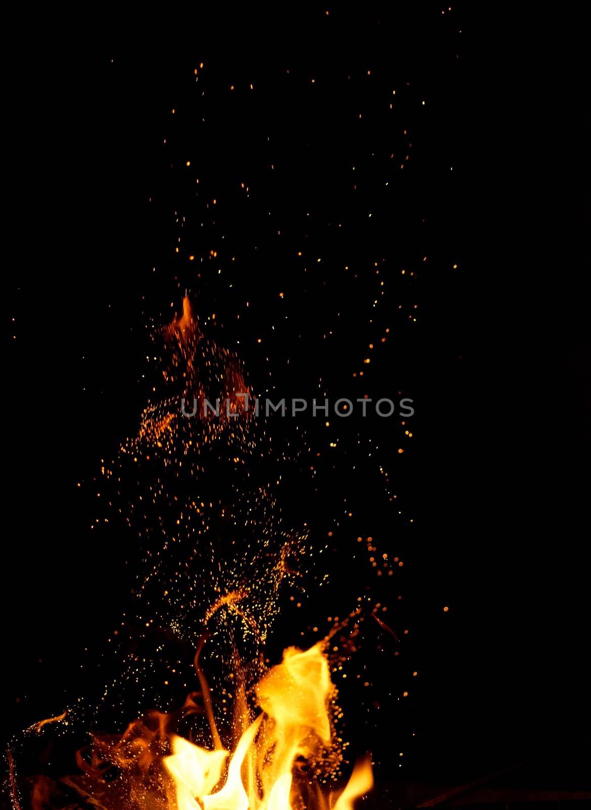 large burning bonfire with flame and orange sparks that fly in different directions on a black background