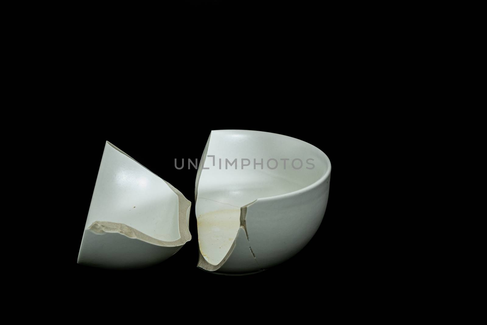 Pieces of broken white ceramic bowl on black background. Copyspace, place for text. Break, fragment. by peerapixs