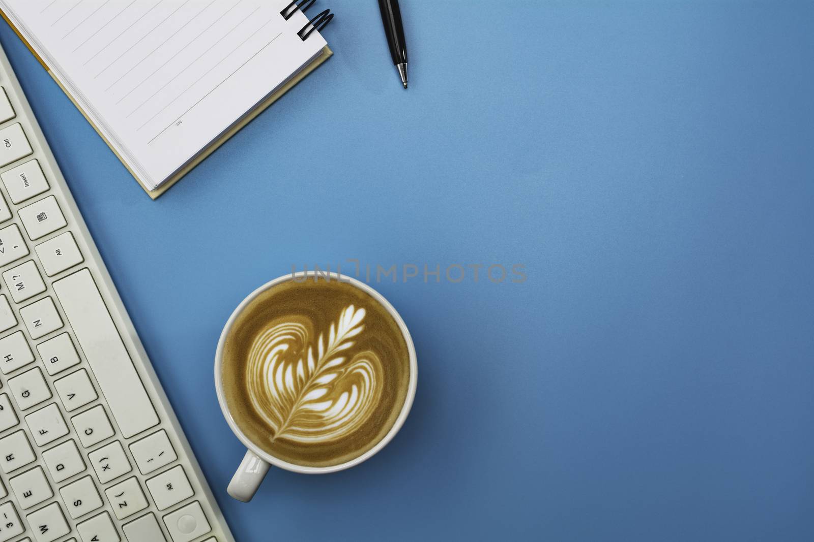 A cup of coffee with keyboard and copy space on blue background. Office desk and drink concept.