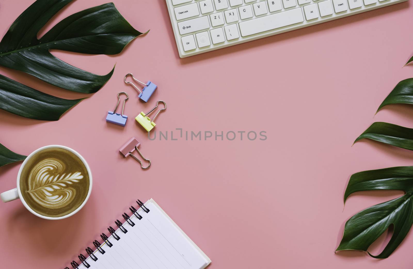 A cup of coffee with keyboard and copy space on pink background. Office desk and drink concept.