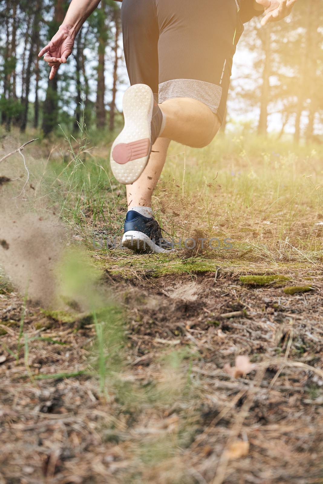 adult man in black shorts runs in the coniferous forest against the bright sun,  concept of a healthy lifestyle and running in the fresh air