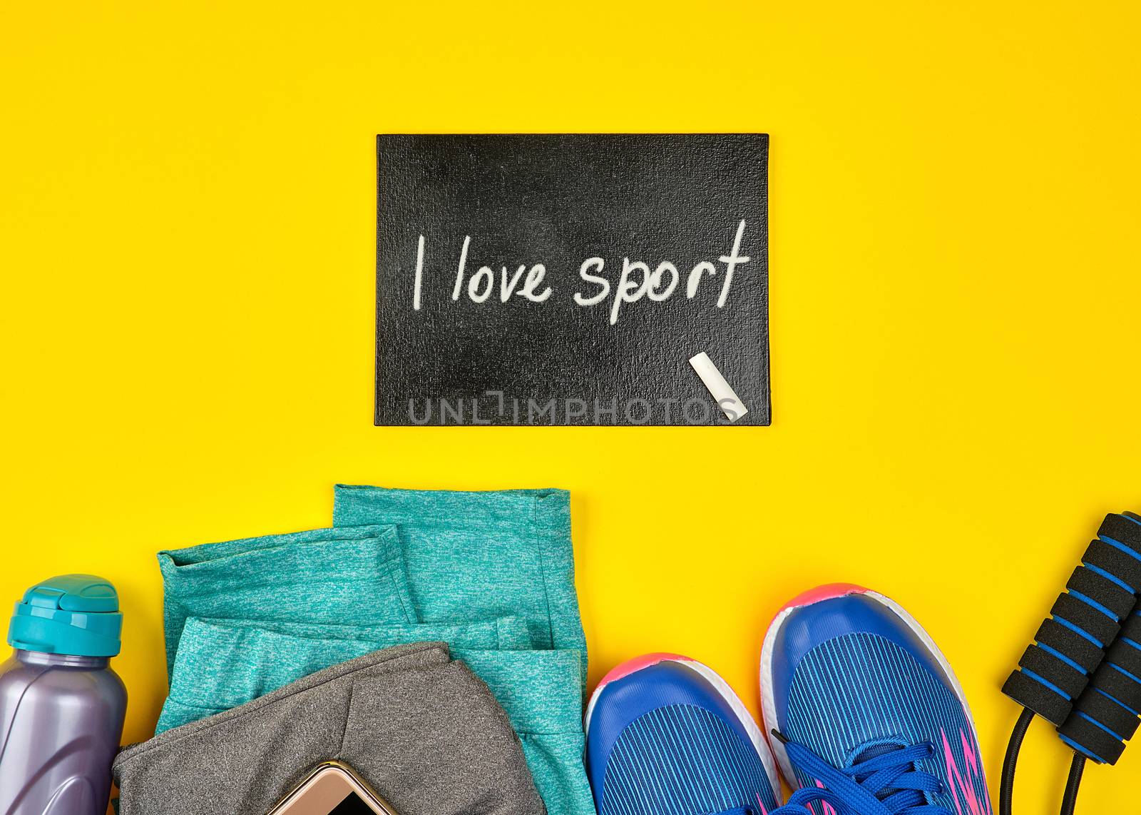 empty blackboard and blue women's sneakers and clothes for sports on a yellow  background, top view, copy space, flat lay