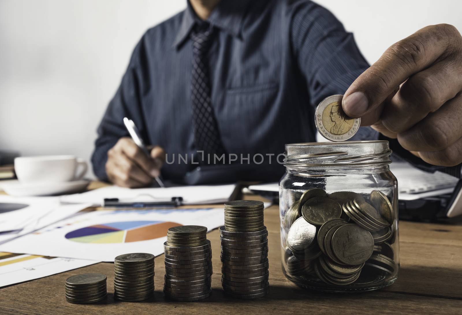 Business man working and writing on notebook with stack of coins for financial and accounting concept.