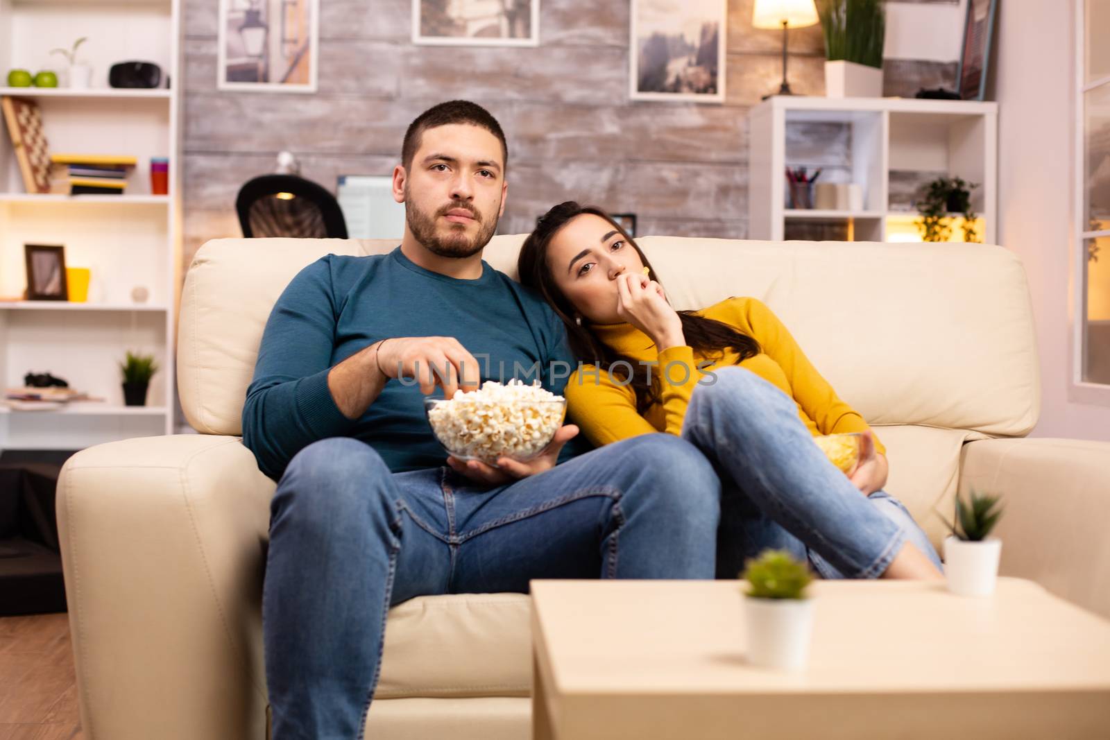 Handsome couple at home eating pop corn and watching TV by DCStudio