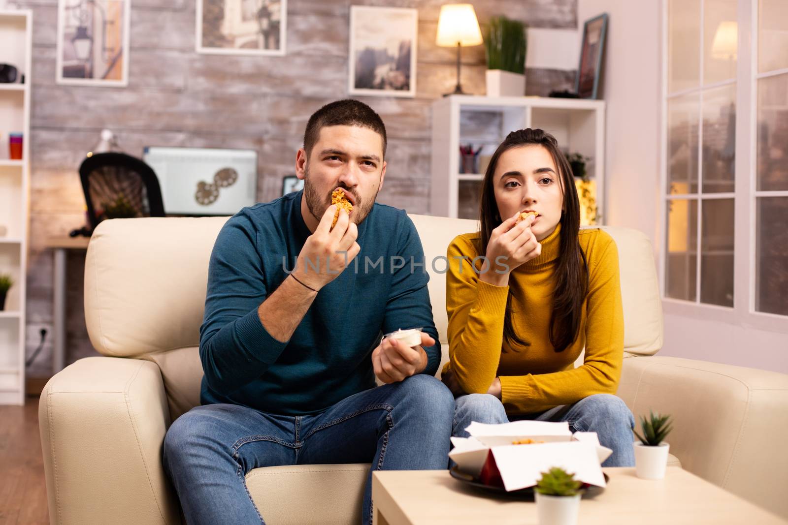 Young couple eating fried chicken in front of the TV by DCStudio